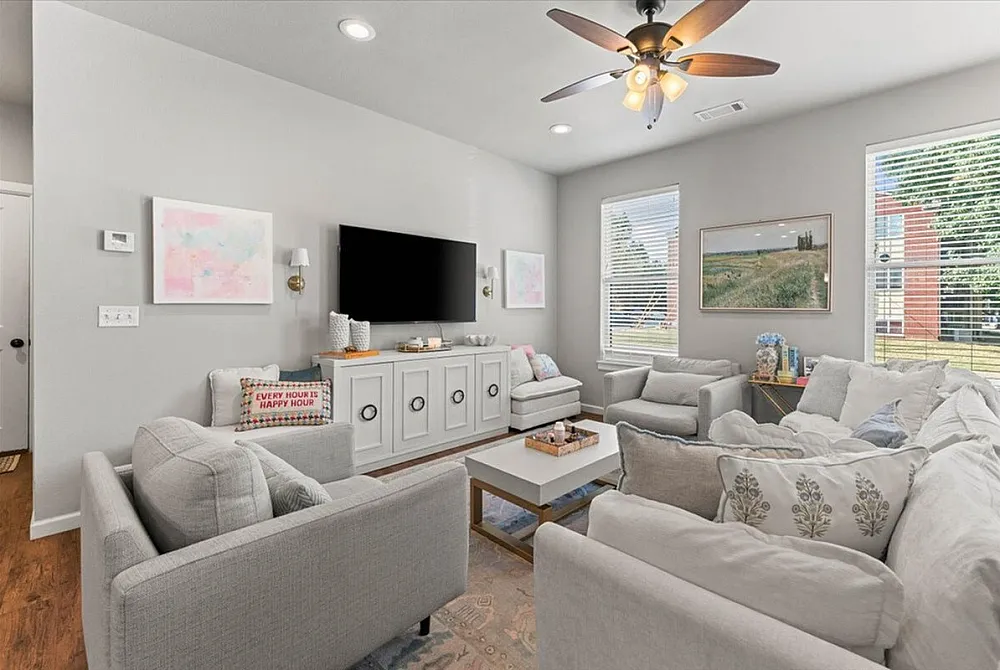 Bright and inviting living room with contemporary gray furniture, sleek TV setup, and elegant ceiling fan, creating a cozy atmosphere with plenty of natural light.