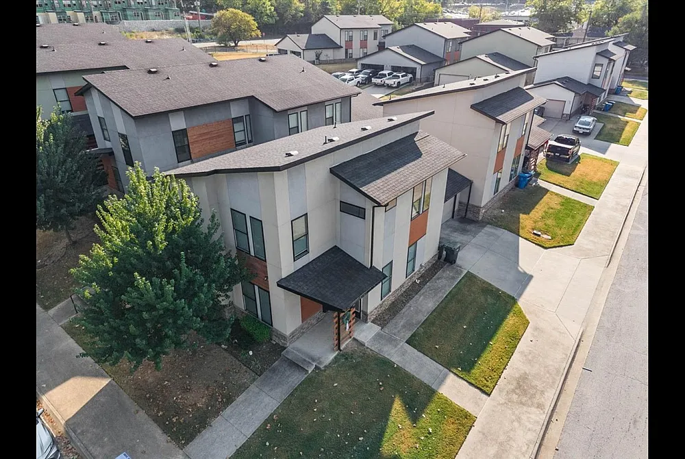 Aerial view of modern townhouses with sleek architecture, lush green landscaping, and convenient parking spaces in a vibrant community setting.