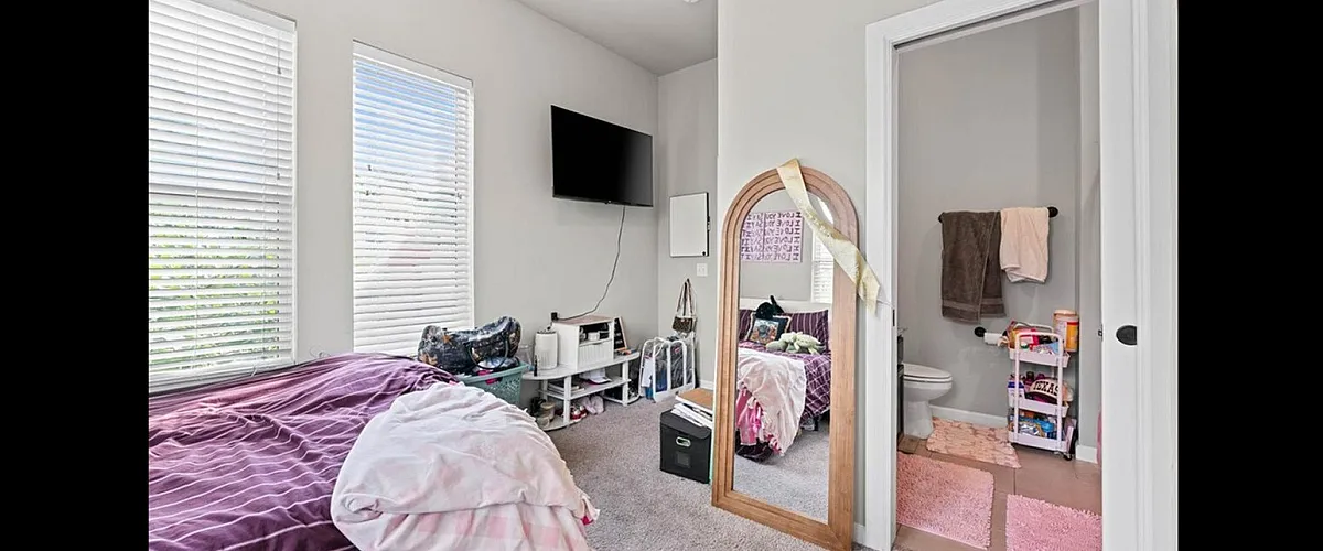 Cozy bedroom with ample natural light, featuring modern decor, plush carpeting, and an ensuite bathroom showcasing a chic pink theme.