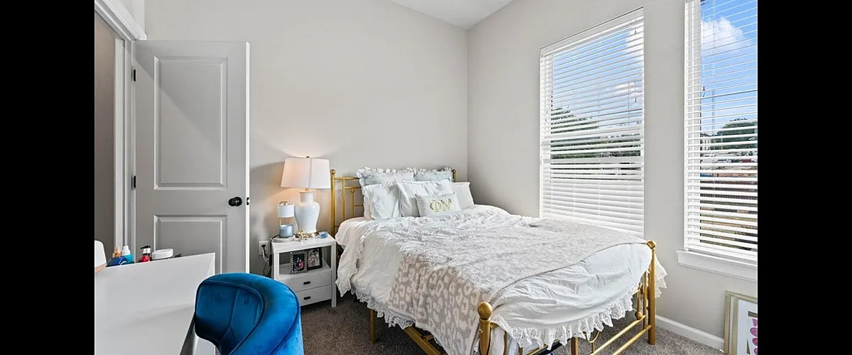 Bright and cozy bedroom with plush bedding, elegant gold bed frame, and modern decor, featuring abundant natural light through large windows.