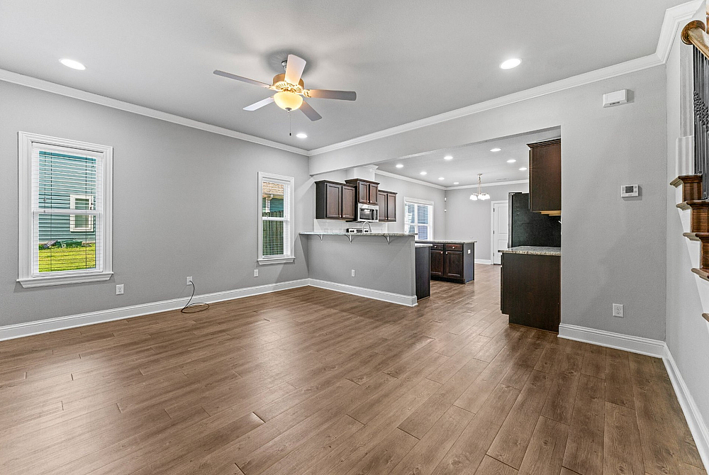 Bright, open-concept living area with elegant wood flooring and modern kitchen featuring dark cabinetry and stainless steel appliances.