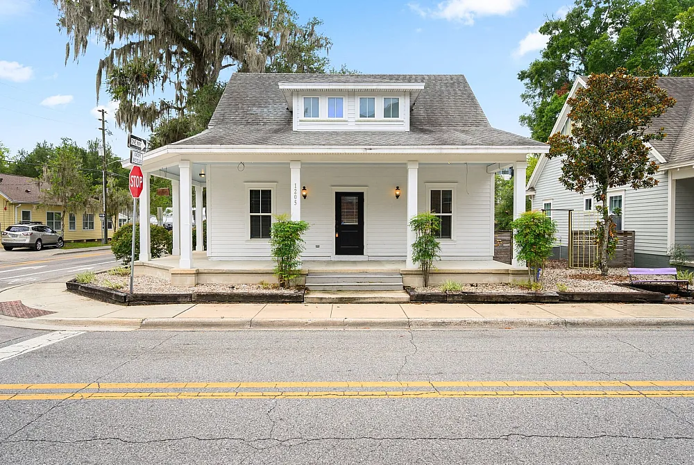 Charming white house with inviting front porch, framed by lush greenery and surrounded by a picturesque neighborhood.