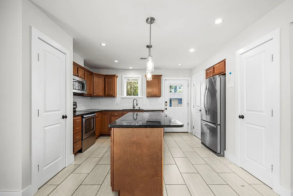Modern kitchen with elegant wooden cabinetry, sleek stainless steel appliances, and a polished granite island countertop. Bright and inviting space featuring tiled flooring and ambient lighting.