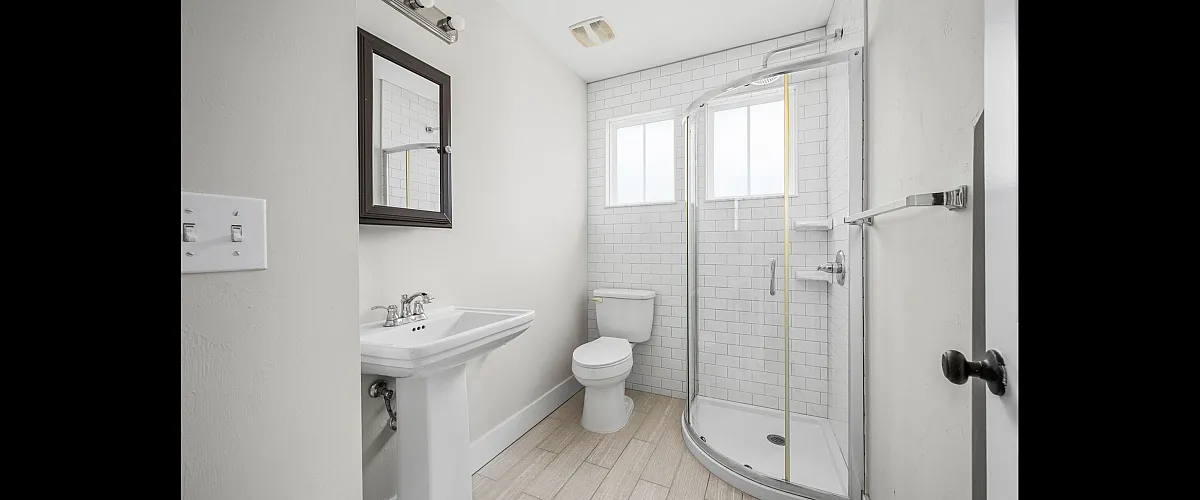 Elegant modern bathroom with crisp white subway tiles, sleek pedestal sink, and stylish corner shower, offering a serene and luxurious ambiance.