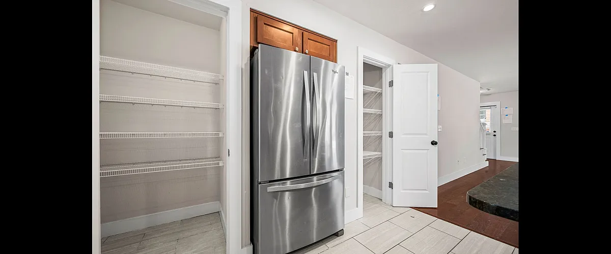 Modern kitchen featuring stainless steel refrigerator, spacious pantry, and sleek tile flooring for a stylish and functional space.
