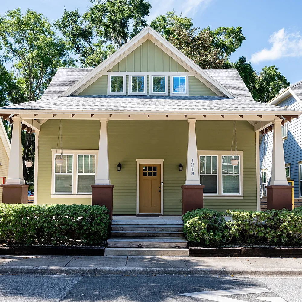 Charming green Craftsman home with inviting front porch, nestled in a lush suburban neighborhood.