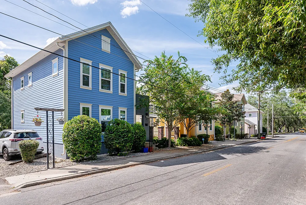 Charming blue two-story house with lush greenery and tree-lined street, offering peaceful suburban living.