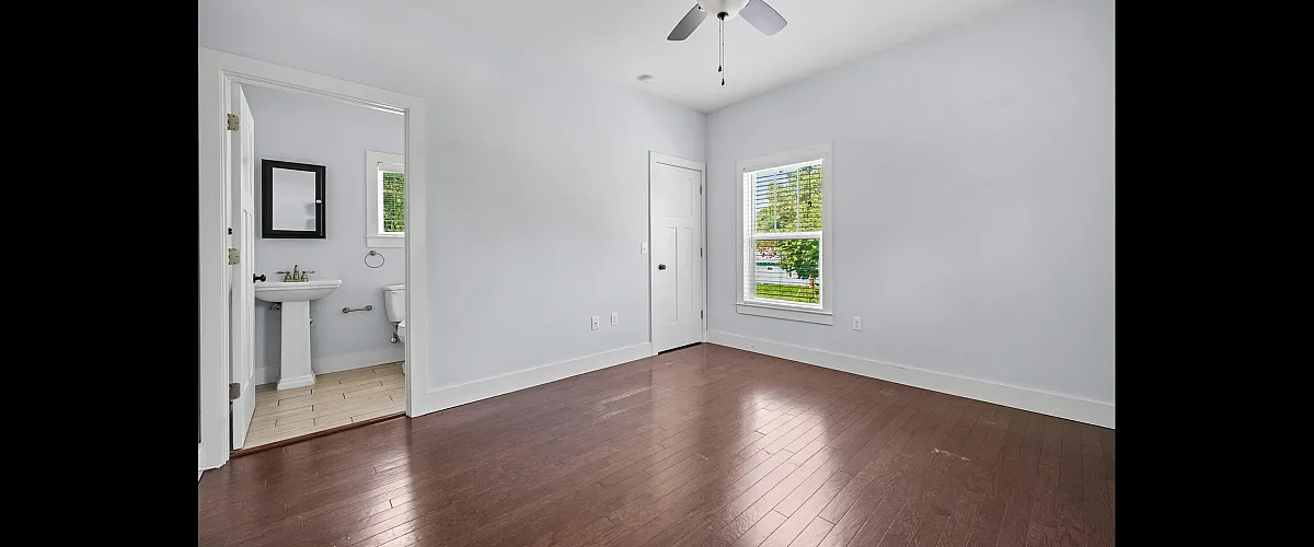Bright, spacious bedroom with elegant hardwood floors, large window, and modern en-suite bathroom for a comfortable living experience.