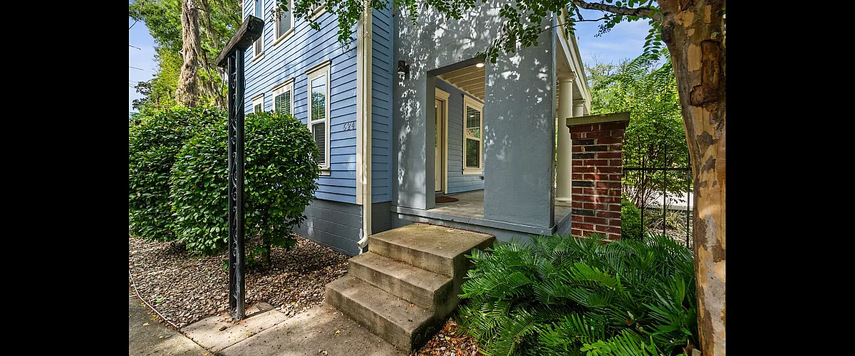 Charming blue exterior of a townhouse with welcoming porch, surrounded by lush greenery.