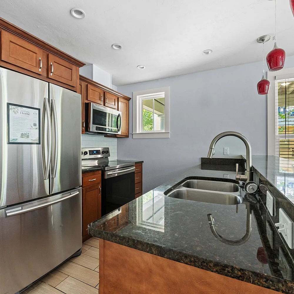 Modern kitchen with stainless steel appliances, rich wood cabinetry, granite countertops, and stylish red pendant lights enhancing a contemporary space.