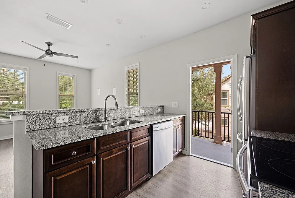 Beautiful kitchen with granite countertops, dark wood cabinets, and stainless steel appliances, opening to a scenic balcony view.