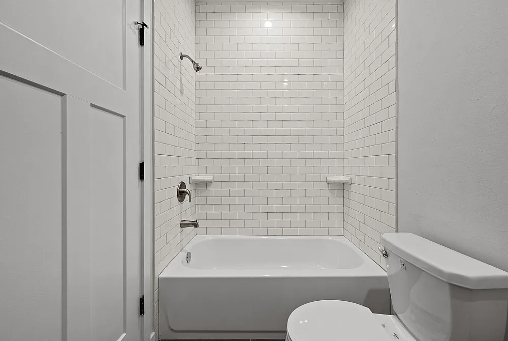 Sleek, modern bathroom featuring elegant white subway tiles, a pristine bathtub, and a contemporary toilet design.