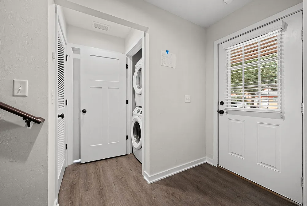 Chic entryway featuring modern wood flooring, a stylish stackable washer-dryer, and bright natural light through a windowed door.