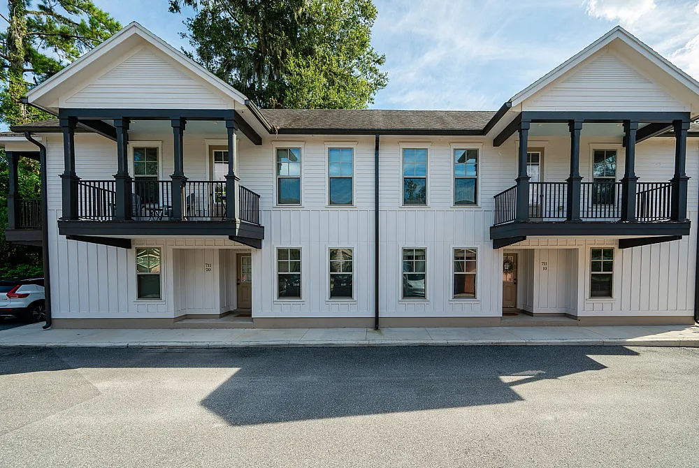 Charming double-story house with elegant white siding and dark rail accents, featuring inviting upper balconies and spacious windows, nestled in a serene environment.