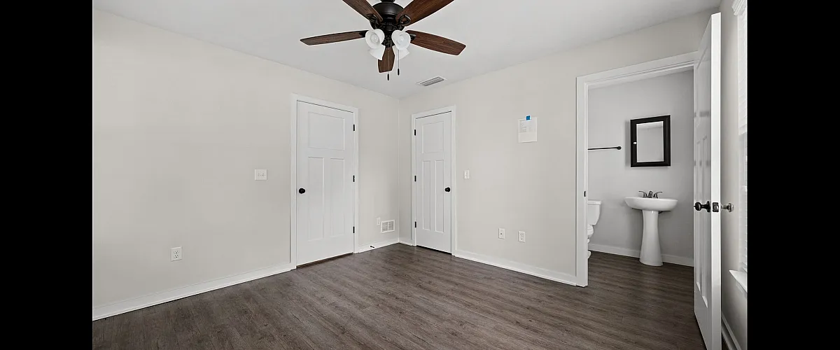 Bright, modern bedroom with elegant wood flooring and a charming ceiling fan, featuring an ensuite bathroom for added convenience.