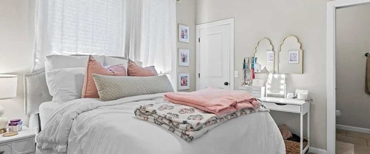 Cozy bedroom with ample natural light, featuring modern decor, plush carpeting, and an ensuite bathroom showcasing a chic pink theme.