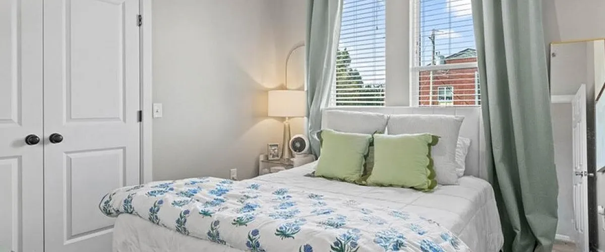 Bright and cozy bedroom with plush bedding, elegant gold bed frame, and modern decor, featuring abundant natural light through large windows.