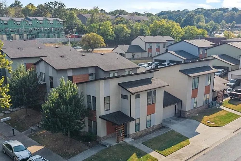 Aerial view of modern townhouses with sleek architecture, lush green landscaping, and convenient parking spaces in a vibrant community setting.