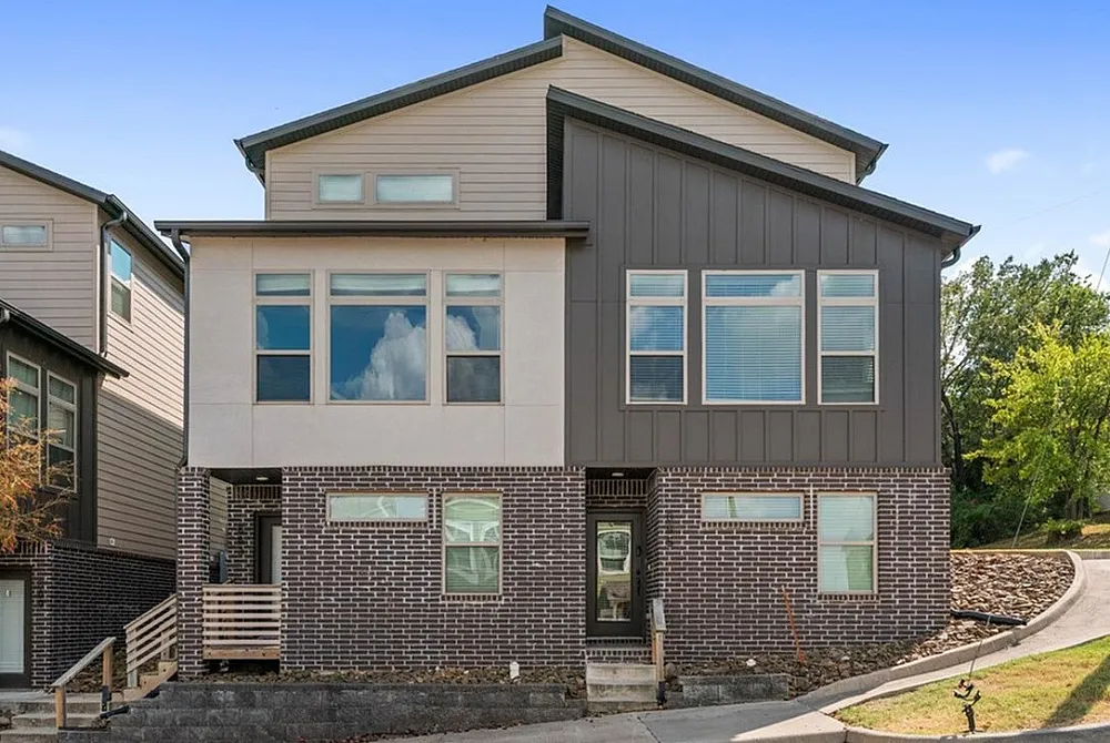 Charming townhouse entrance with a modern facade, surrounded by lush greenery and a neatly paved driveway.