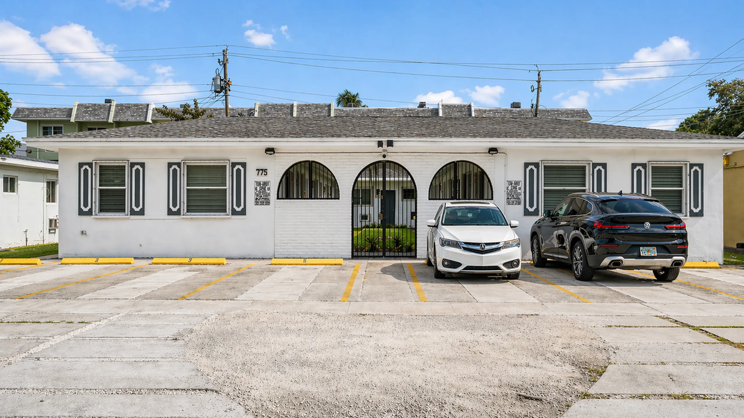 Charming modern apartment building with stylish arched entryways, ample parking, and inviting curb appeal under a bright blue sky.