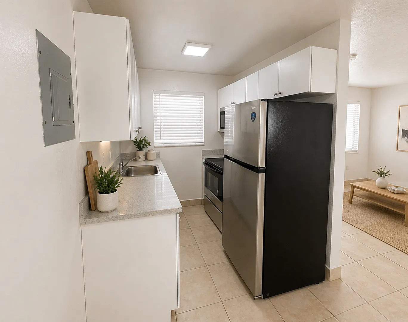 Modern kitchen with sleek stainless steel appliances, bright window light, and elegant potted plants, leading into a cozy living room with stylish decor.