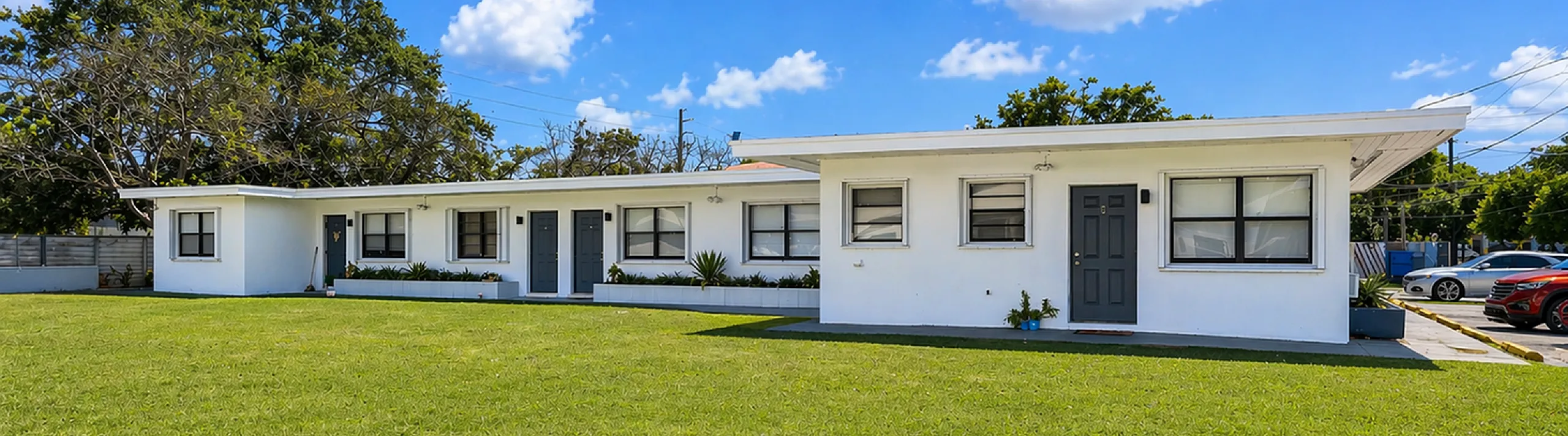 Charming white residential building with multiple units, surrounded by a lush green lawn and set against a clear blue sky.