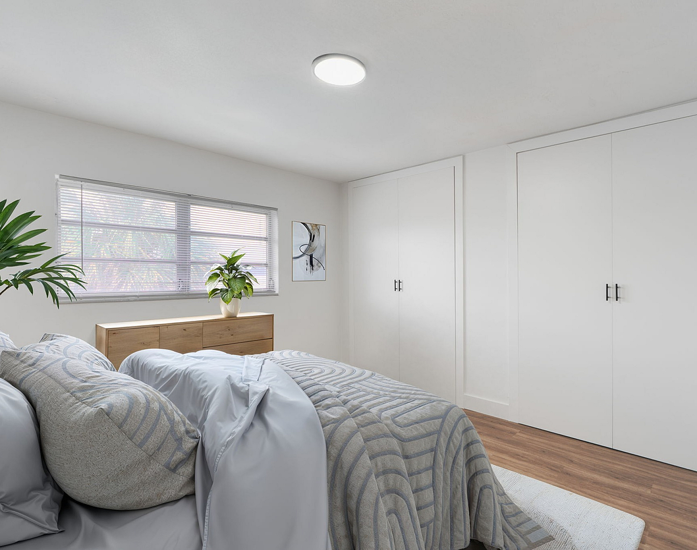 Bright and inviting bedroom featuring cozy bedding, stylish wooden dresser, and ample closet space, highlighted by a large window and elegant decor.