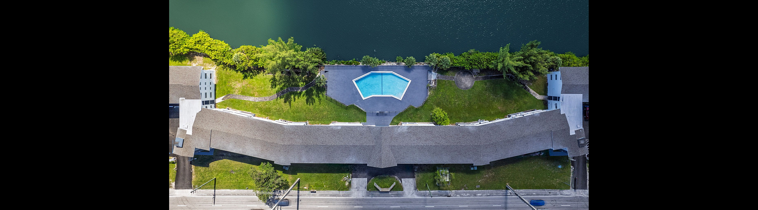 Breathtaking aerial view of a waterfront apartment complex with a pristine hexagonal swimming pool and lush greenery, offering serene lakeside living.