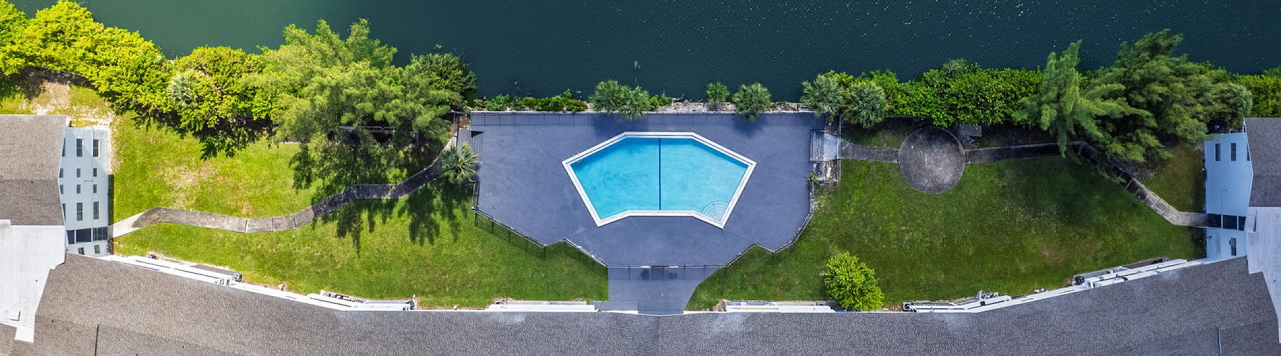 Aerial view of a stylish apartment complex with a unique geometric pool, lush greenery, and a waterfront setting.