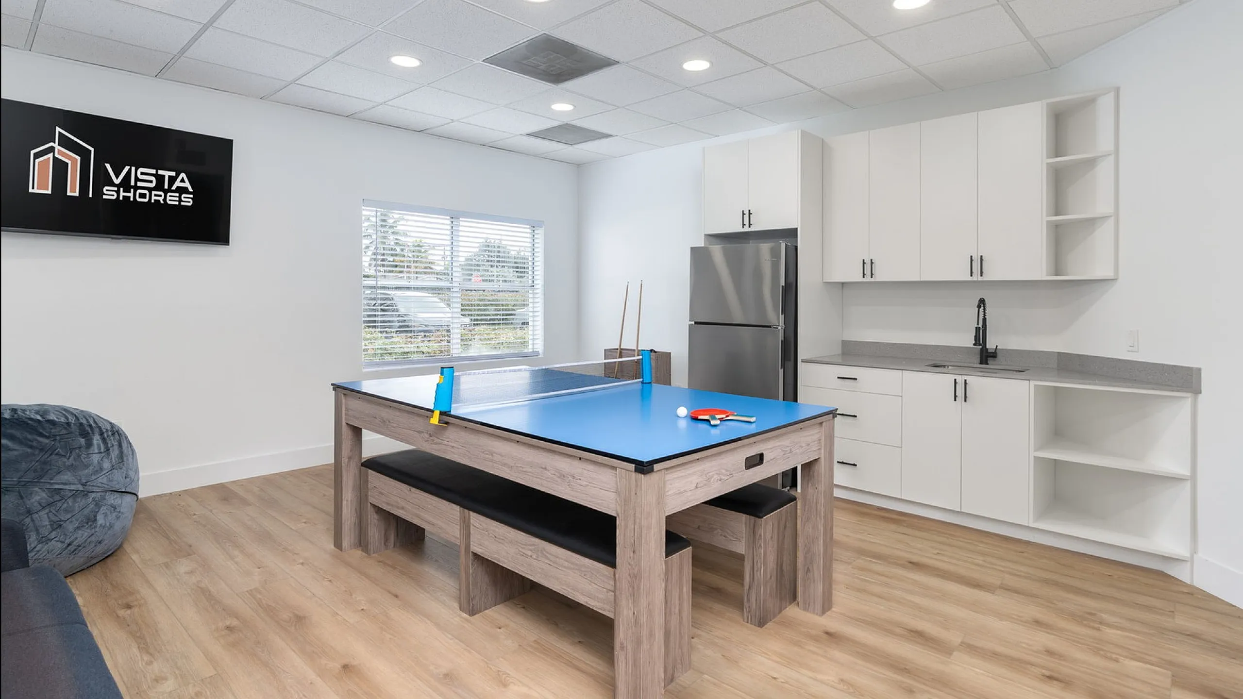 Modern entertainment room at Vista Shores featuring a sleek ping pong table, spacious kitchenette, and cozy seating area with natural light.
