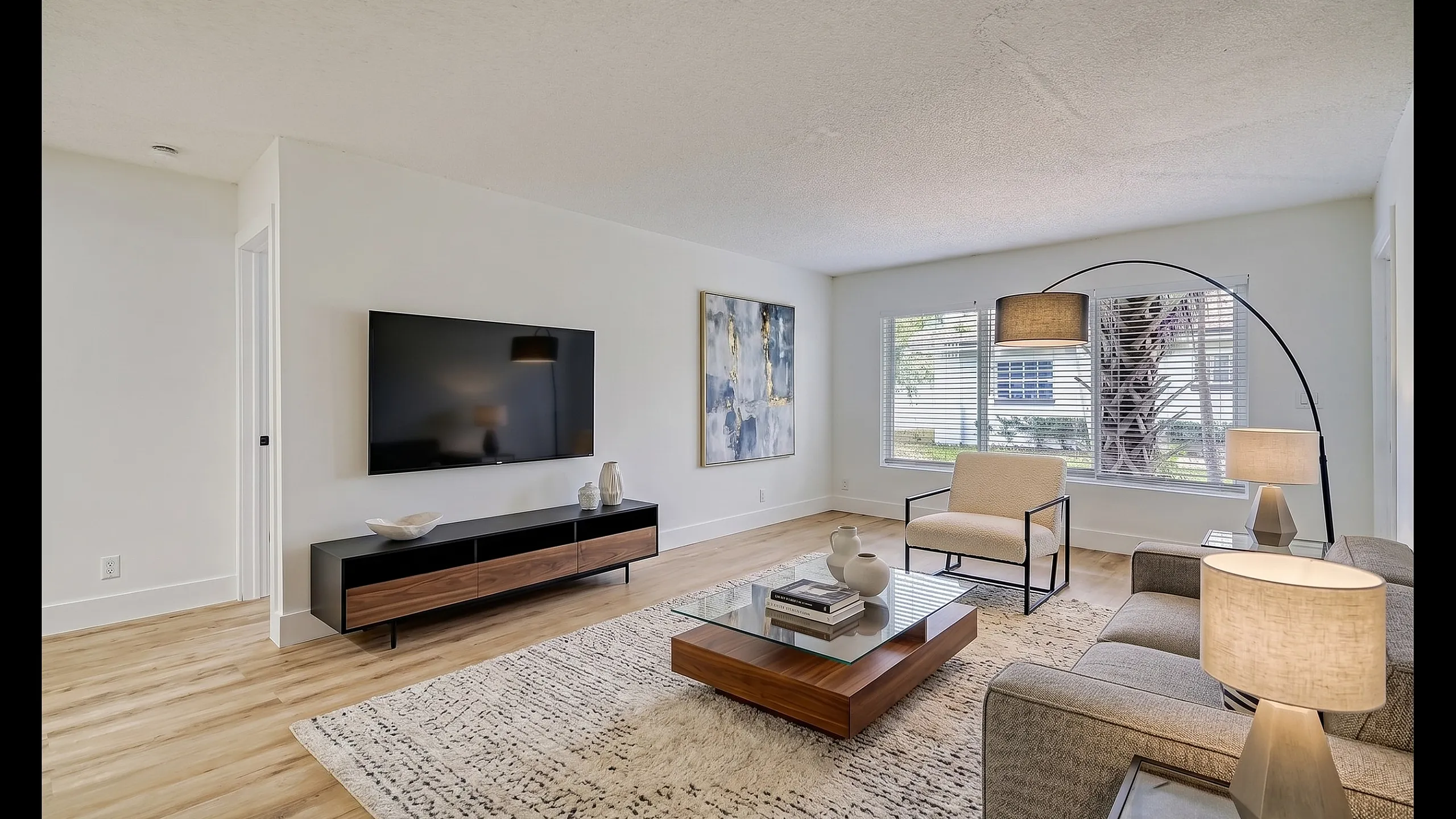 Modern living room with elegant decor, featuring a large flat-screen TV, sleek furniture, and a spacious window for natural light.