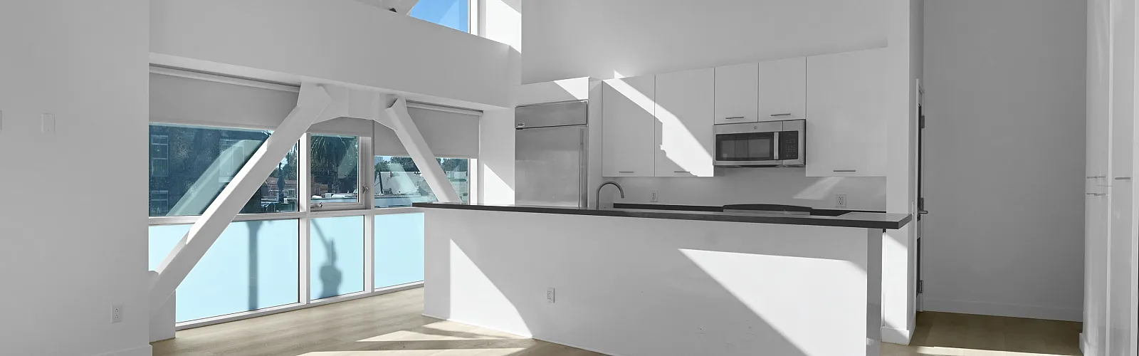 Open-concept loft with large windows, high ceilings, and a minimalist kitchen.