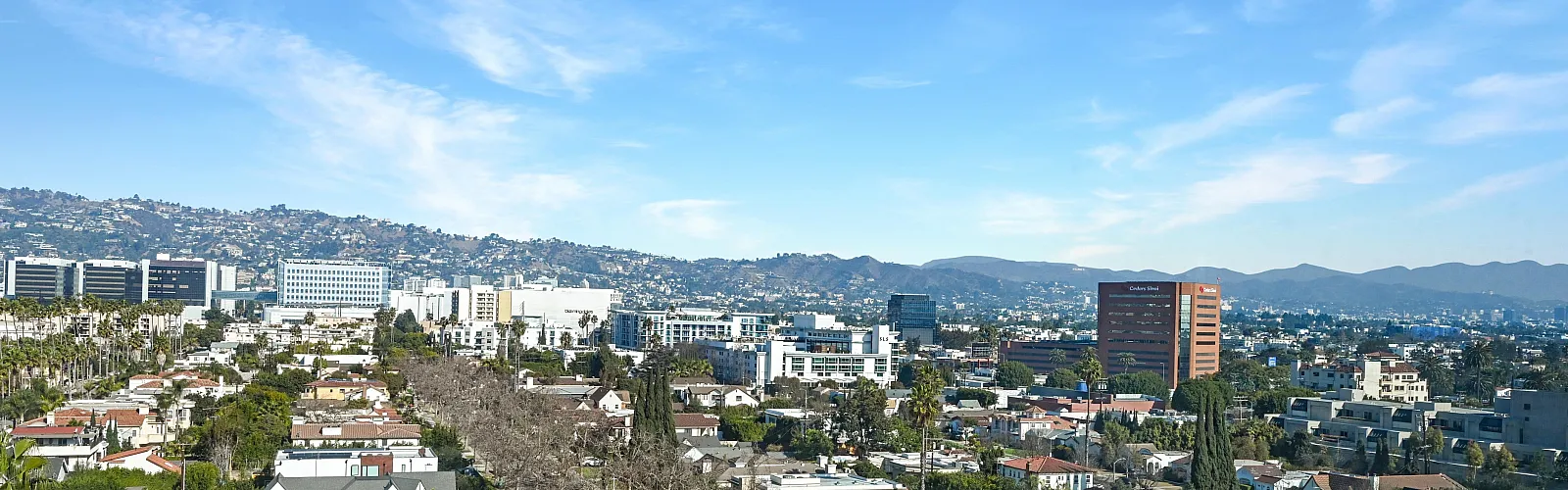 Panoramic view of a vibrant cityscape with modern buildings and distant rolling hills under a clear blue sky.