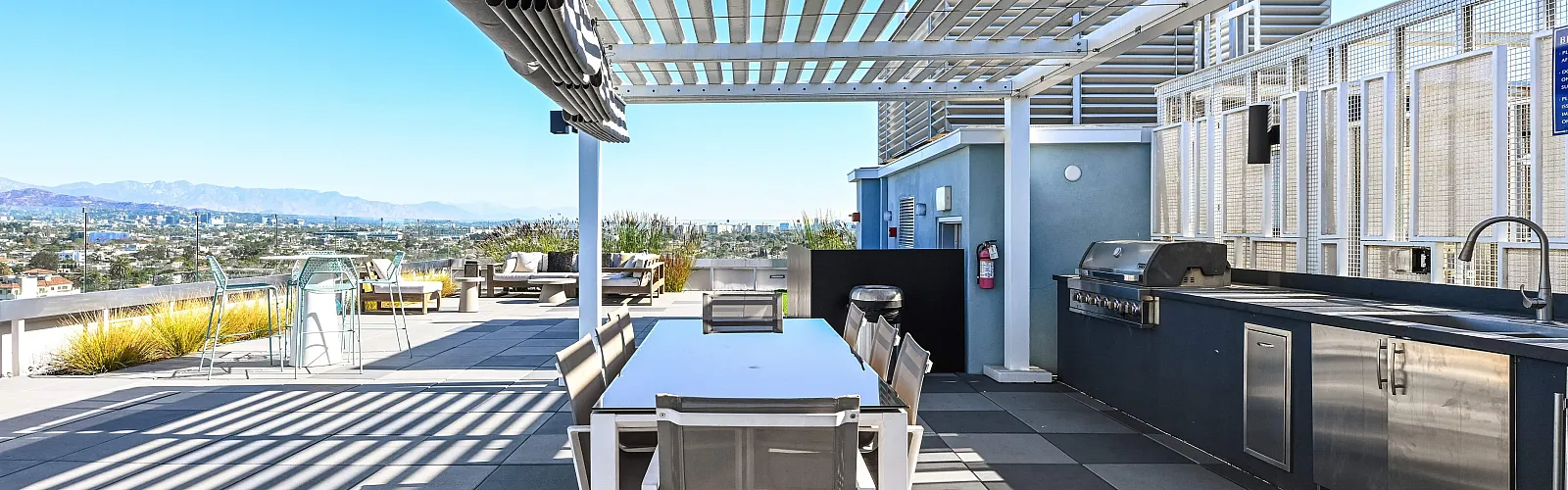 Modern rooftop terrace featuring a sleek outdoor dining area, grill, and panoramic city view.