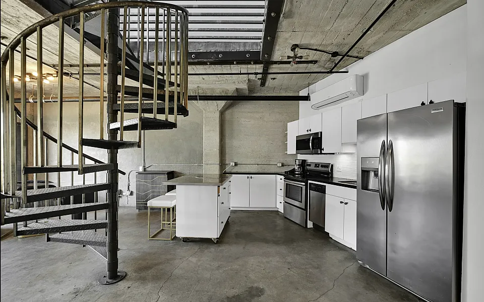 Chic kitchen area featuring modern appliances, white cabinetry, and a spiral staircase in an urban loft setting.