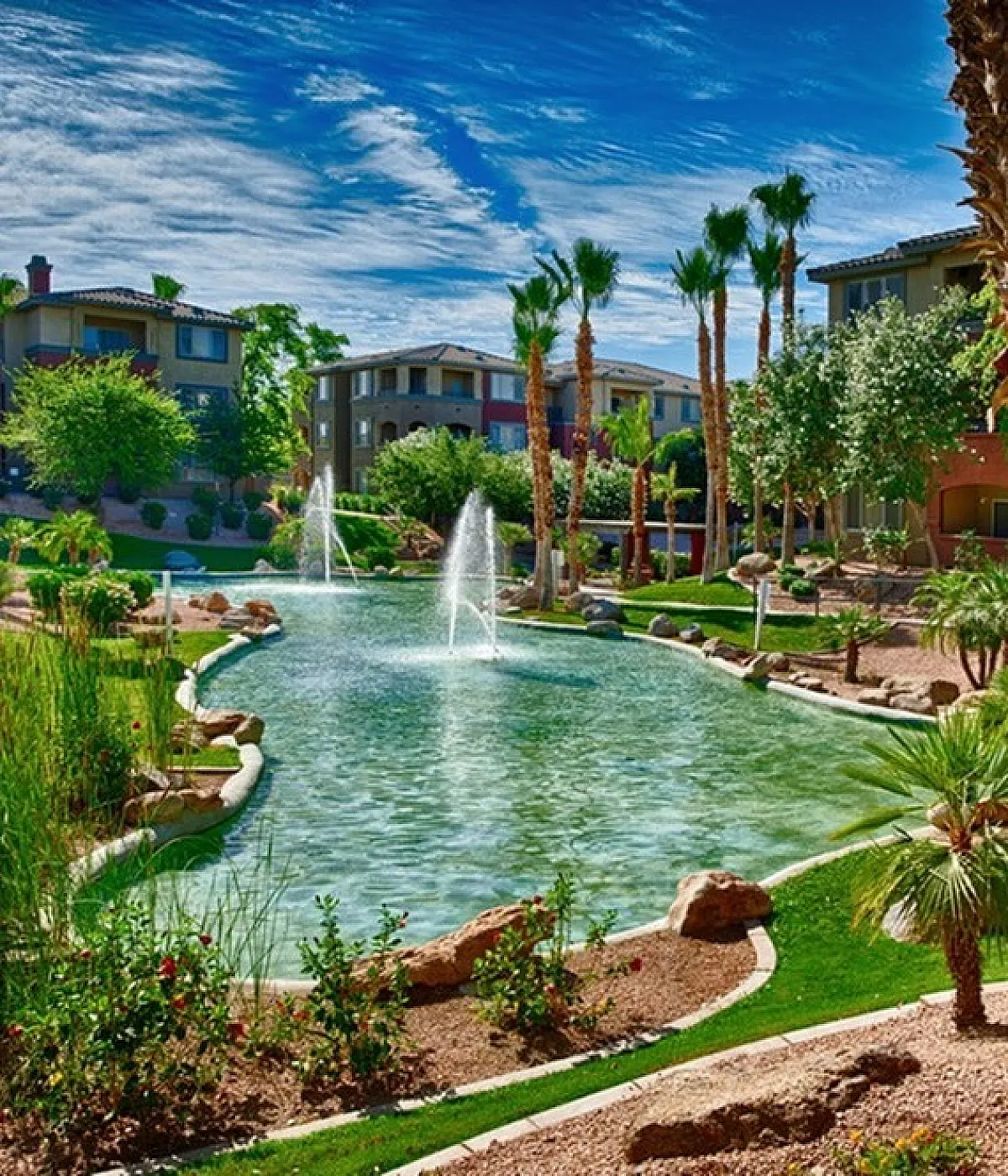 Luxury apartment complex featuring lagoon-style pool, lush landscaping, and elegant architecture under a clear blue sky.