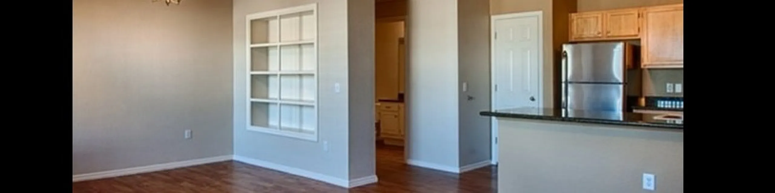 Modern open-concept apartment with polished wood floors, spacious living area, and sleek kitchen featuring stainless steel appliances.