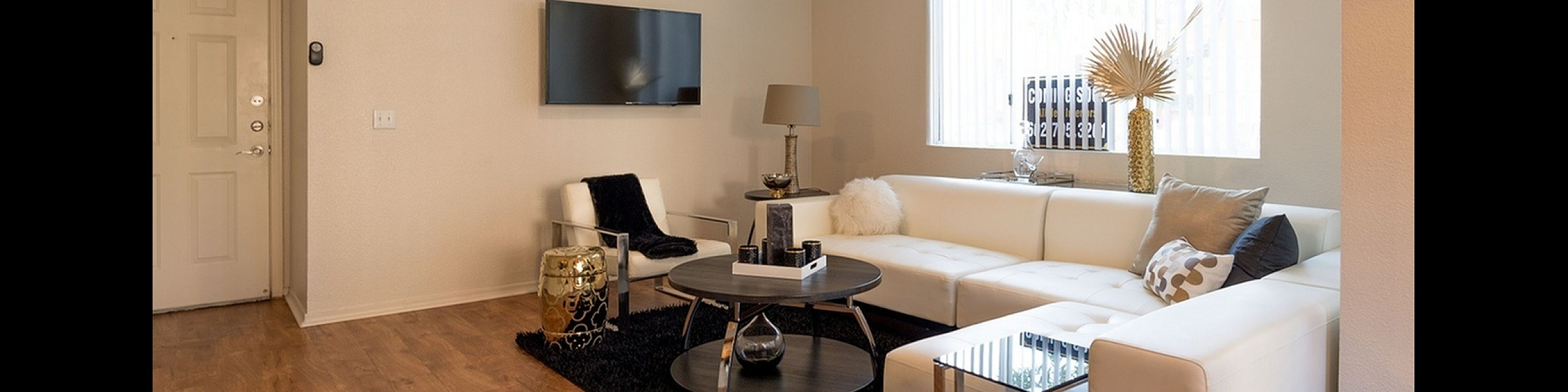 Contemporary living room with elegant white sectional sofa, modern decor, and warm wooden flooring bathed in natural light.