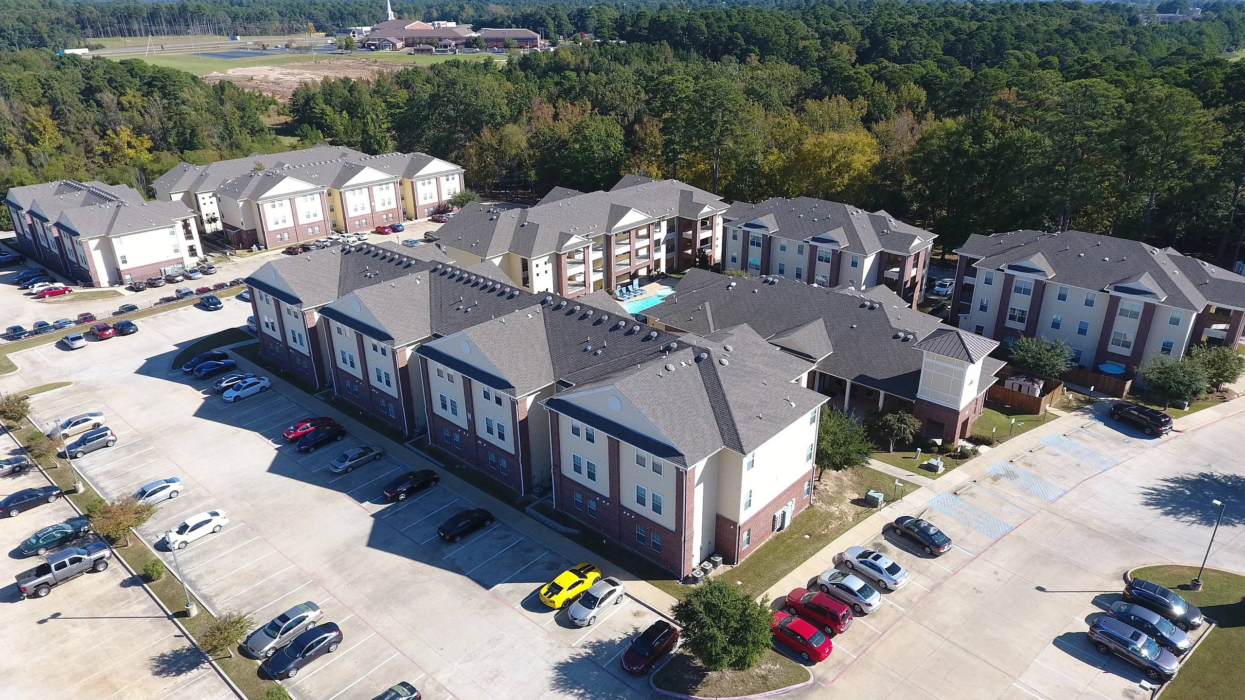 Aerial view of a modern apartment complex surrounded by lush greenery, featuring spacious parking and contemporary architecture.