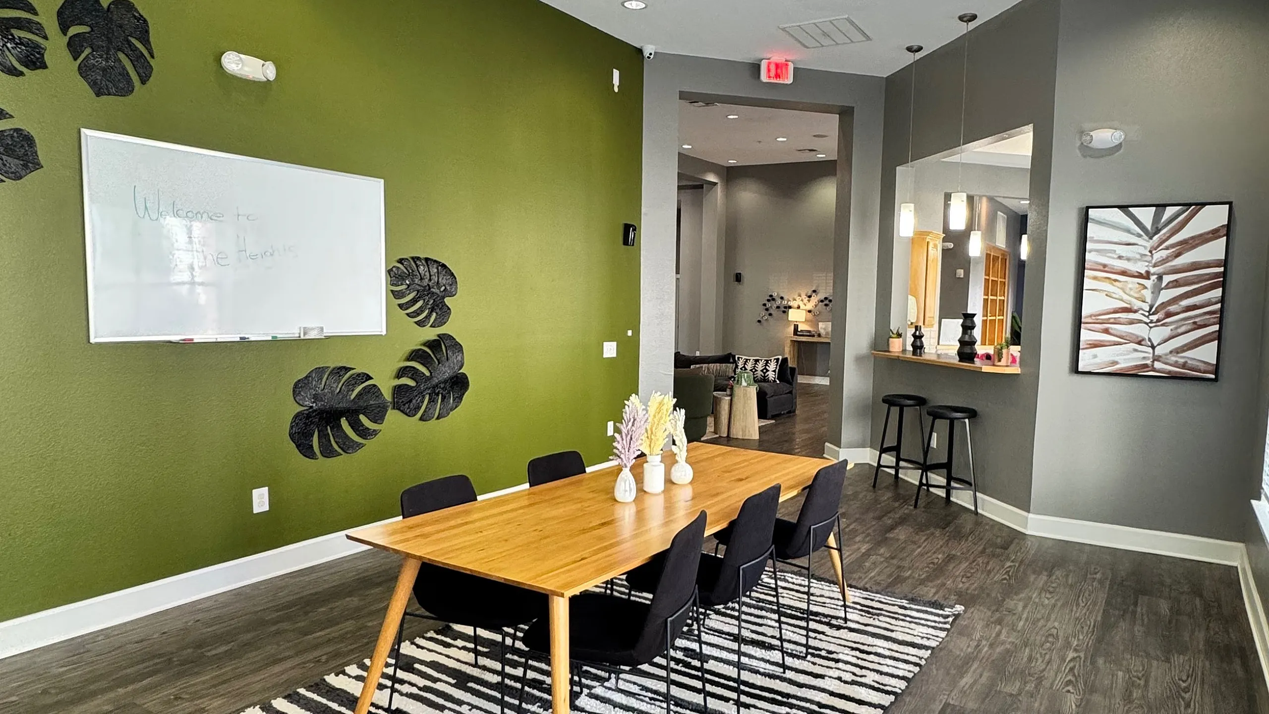 Modern meeting space with vibrant green accent wall, stylish wooden table, and sleek black chairs on a chic striped rug.