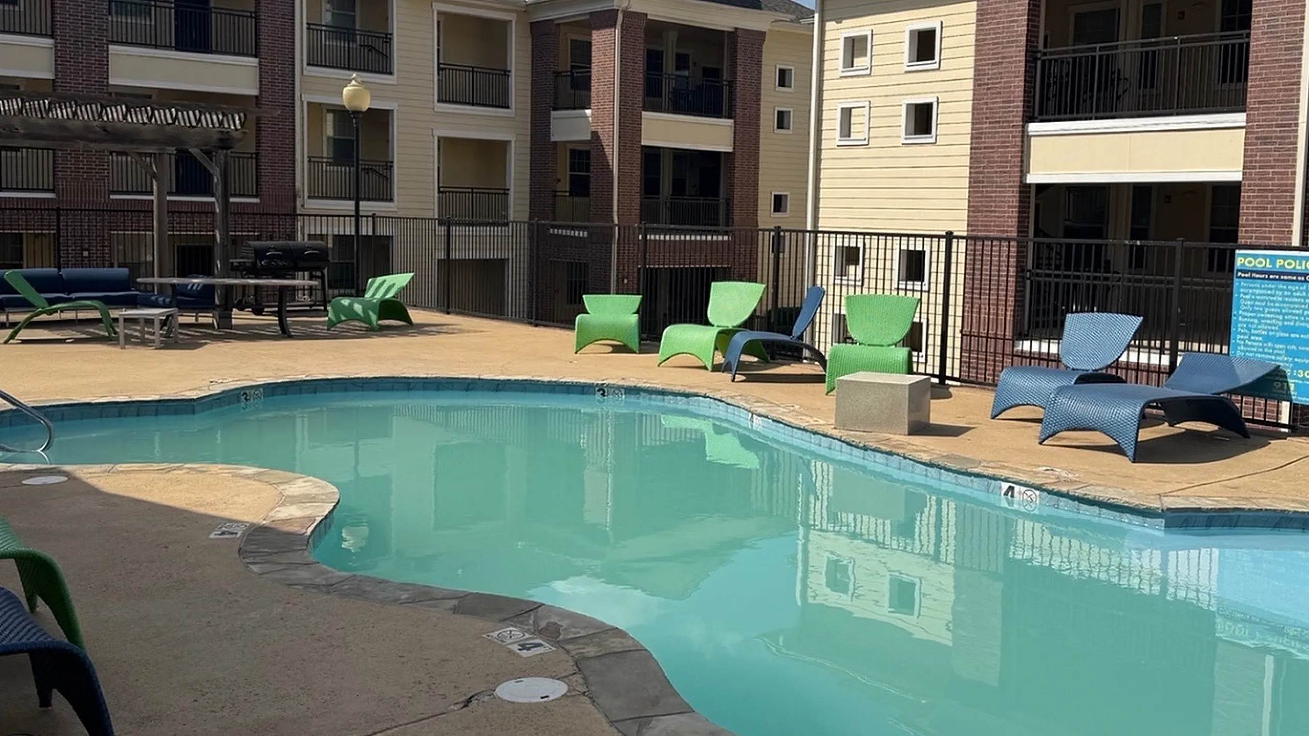 Inviting apartment complex with a sparkling pool, modern architecture, and vibrant lounge chairs, perfect for relaxing under clear blue skies.