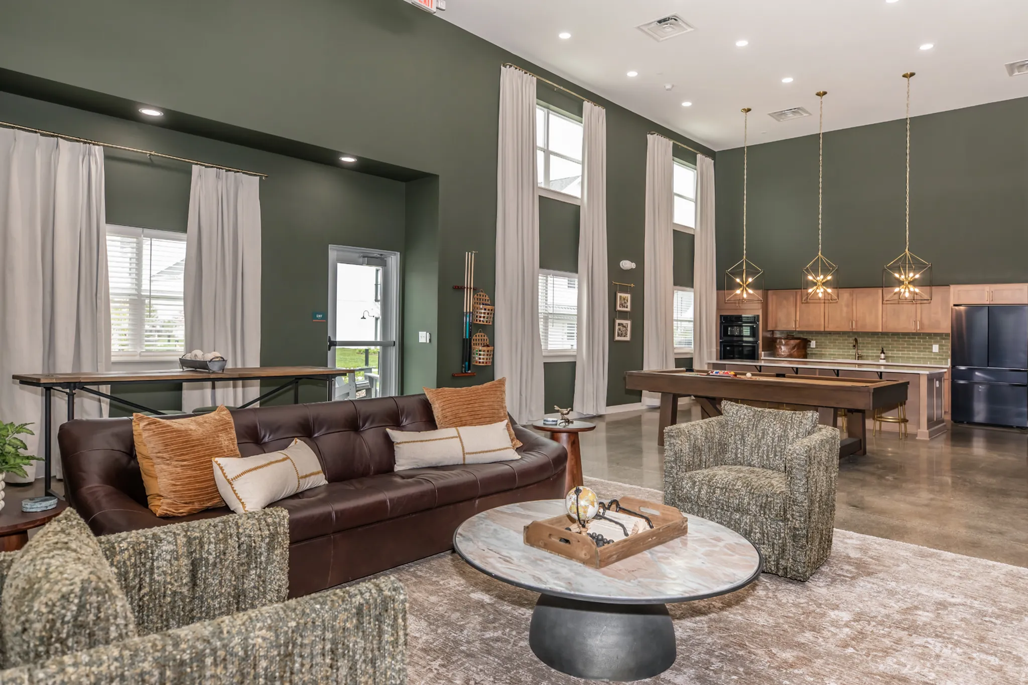 Elegant open-concept living room with high ceilings, luxurious leather sofa, and modern kitchen with chic lighting fixtures.