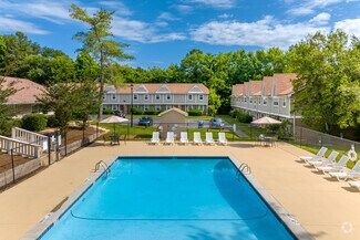 Inviting outdoor pool area with lounge chairs and lush greenery, perfect for relaxation in a picturesque residential complex.