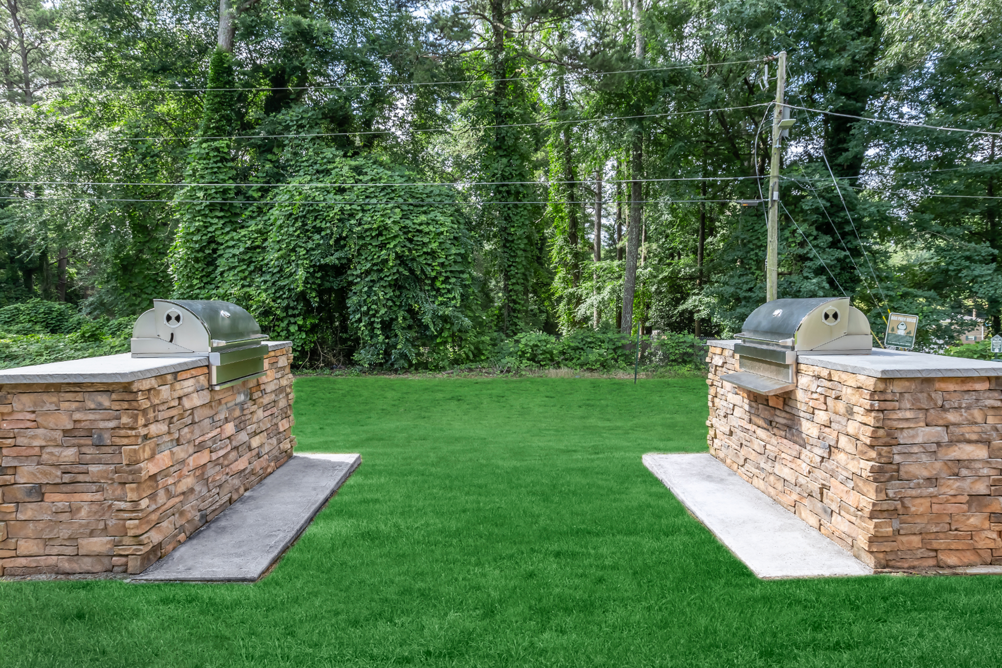 Inviting outdoor space featuring dual stone barbecue grills set in a lush green garden, ideal for entertaining.