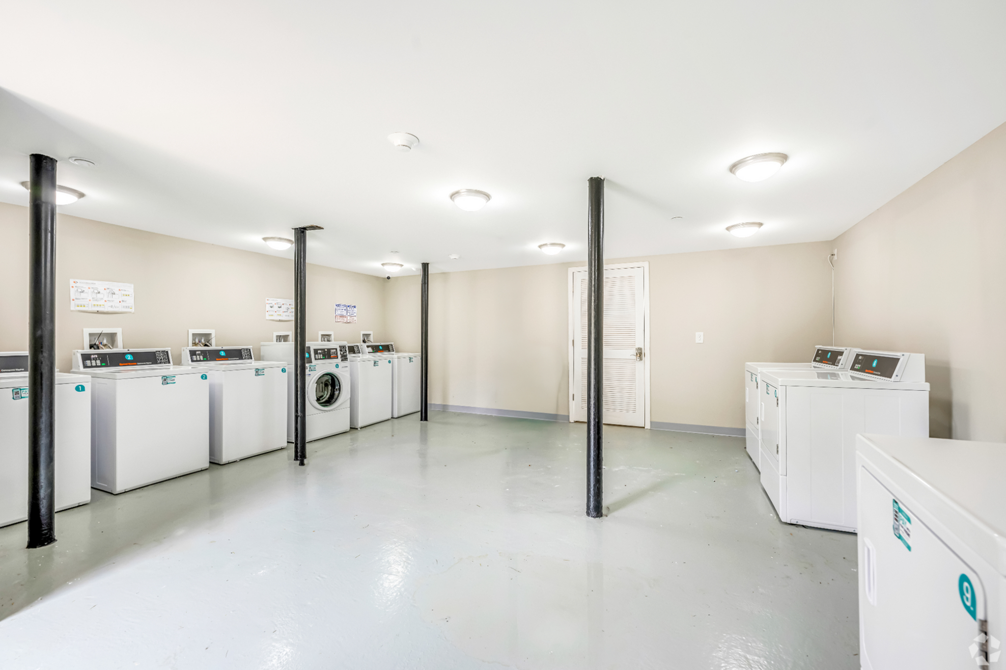 Bright and spacious communal laundry room featuring modern washing machines, ample lighting, and clean facilities.