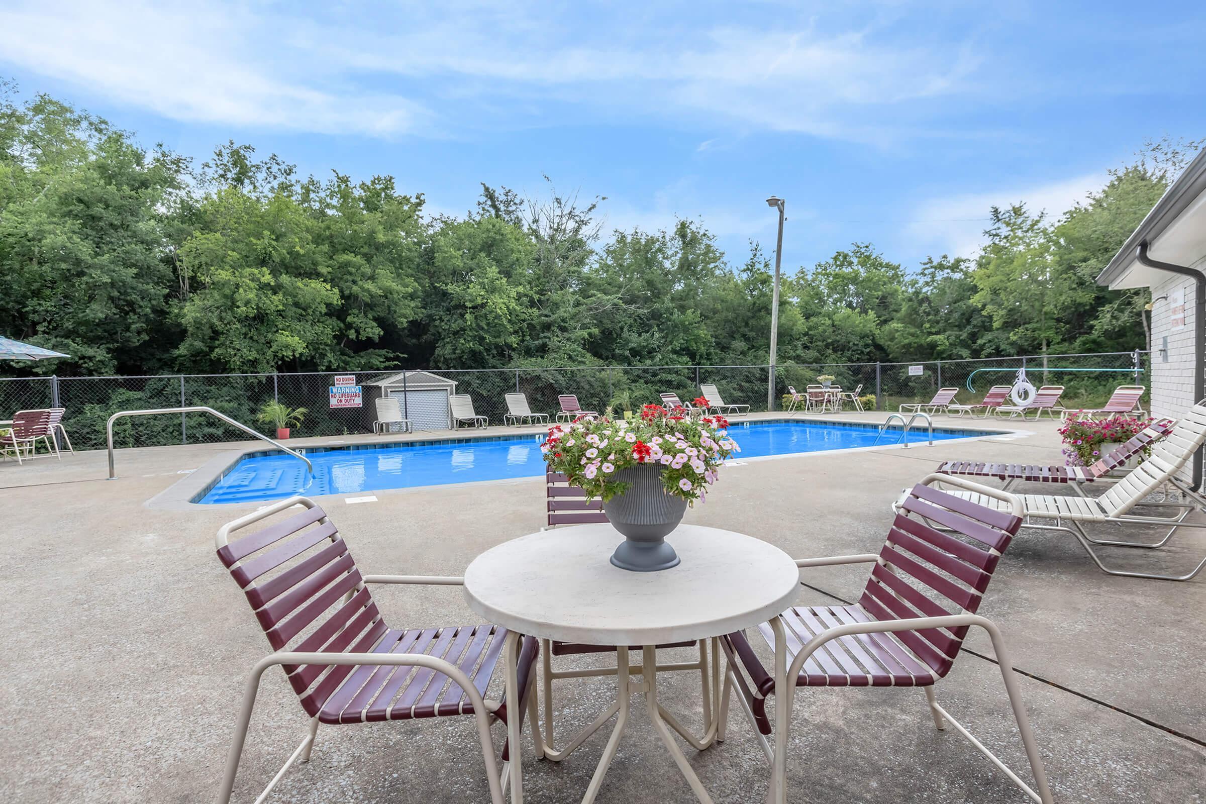 Charming outdoor pool area with cozy seating, surrounded by lush greenery and featuring vibrant floral arrangements.