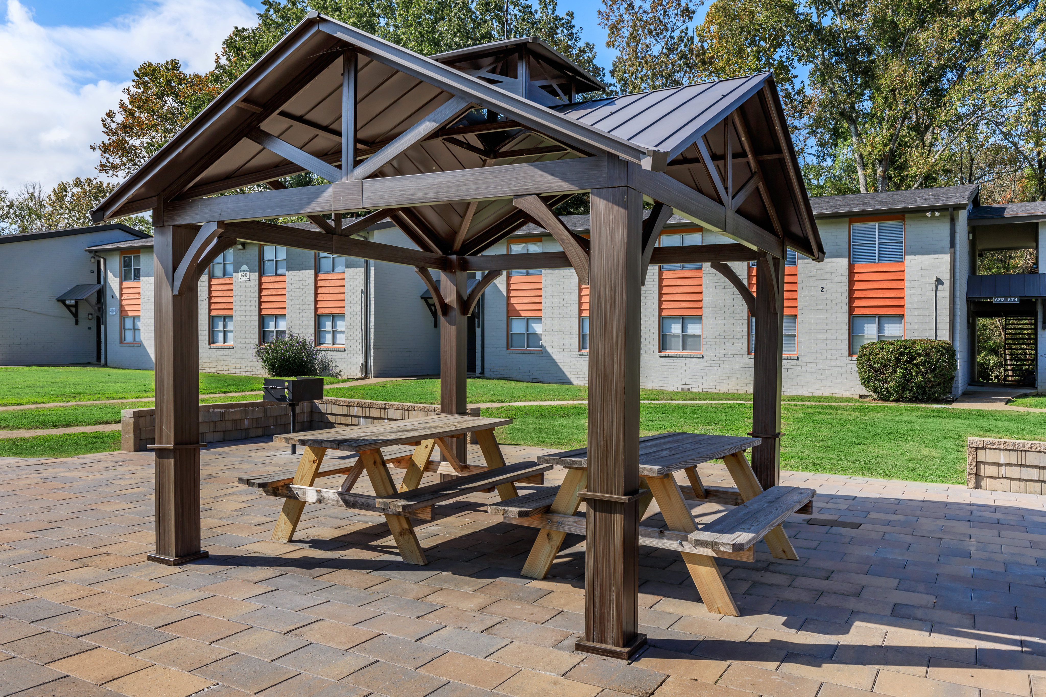 Charming outdoor pavilion with picnic tables on a sunny patio, perfect for gatherings and relaxation, surrounded by lush greenery.