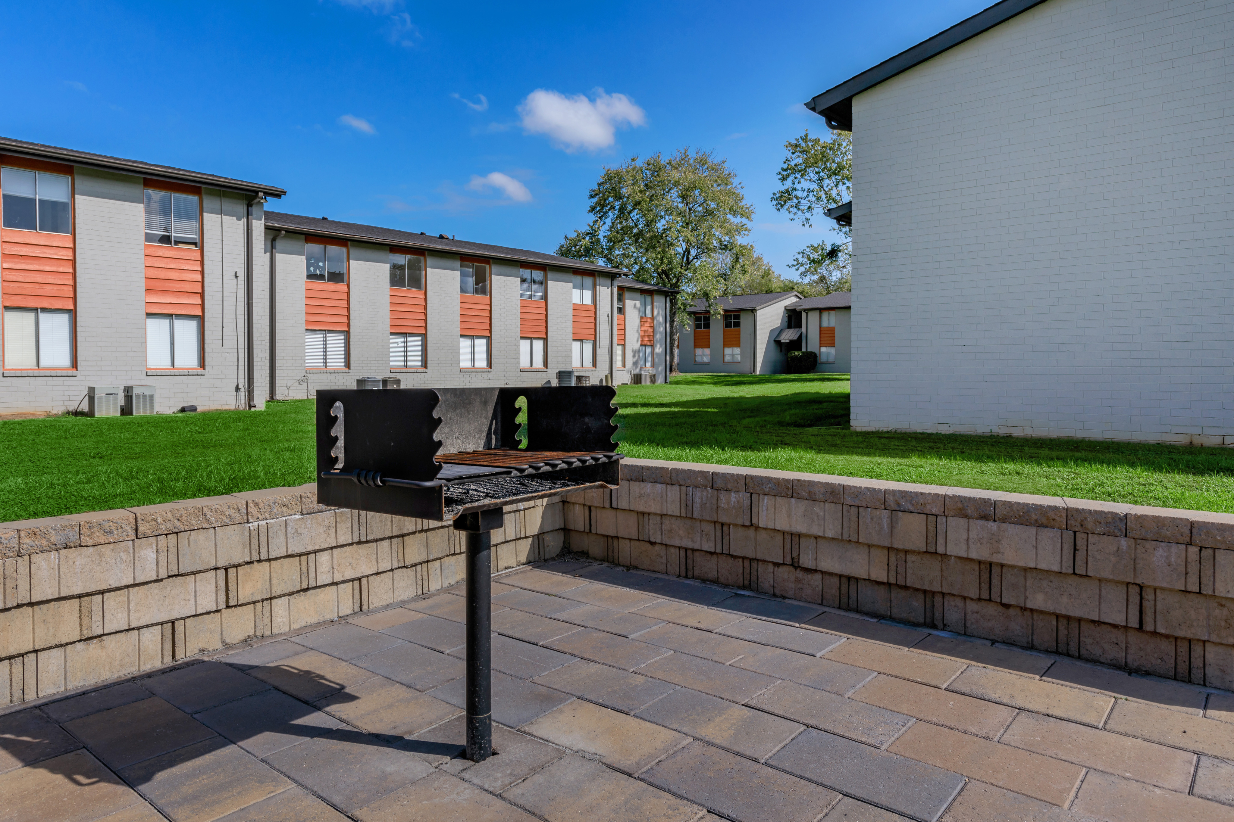 Charming outdoor area with a built-in grill, perfect for entertaining, set alongside modern apartment buildings with lush green lawns.