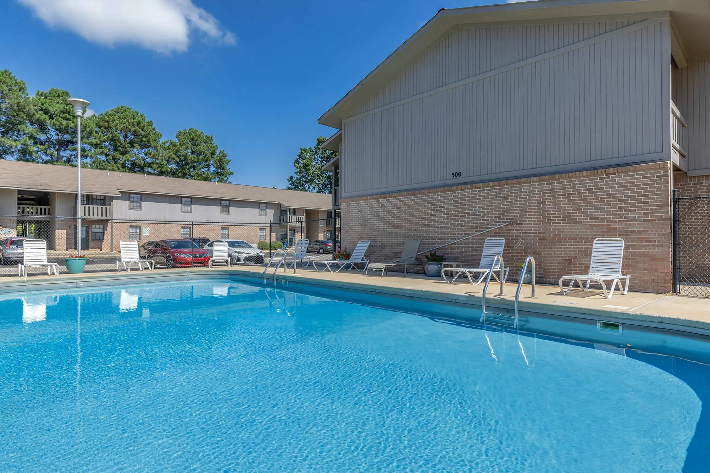 Inviting apartment complex featuring a sparkling outdoor pool surrounded by lounge chairs, perfect for relaxation and leisure.