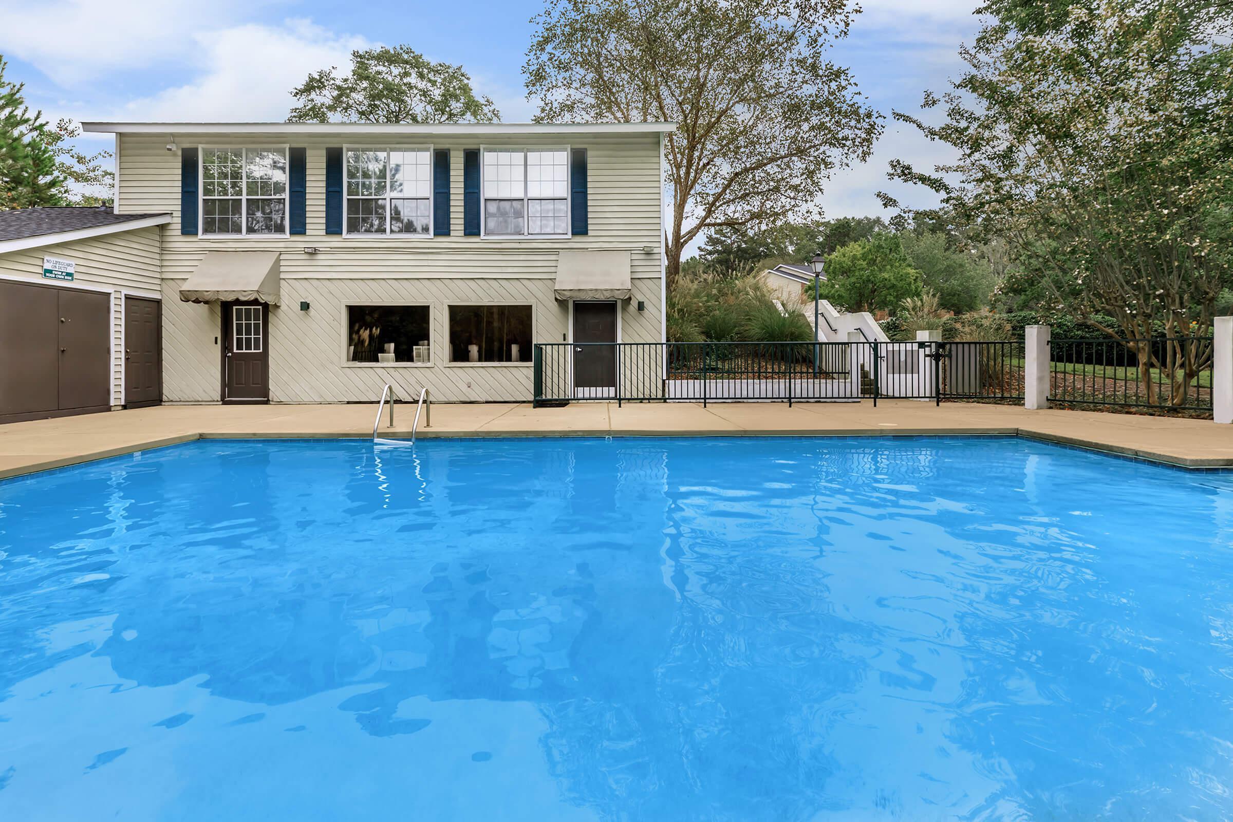 Inviting outdoor pool area with a refreshing blue swimming pool, surrounded by lush greenery and a charming two-story residential building.